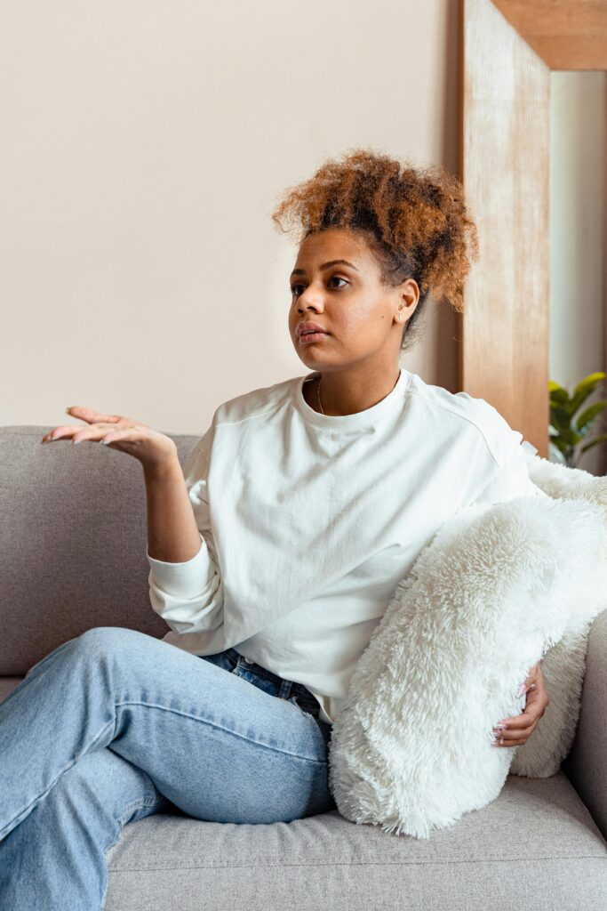 A woman in a white sweater sits on a couch discussing during a therapy session.