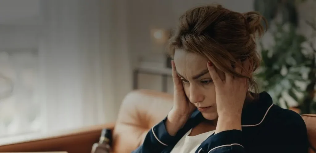 Woman sitting with hands on her temples, appearing stressed and overwhelmed, representing anxiety and emotional distress